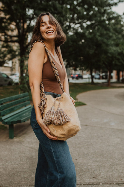 Woman laughing and smiling at camera while showing cream tan colored boho crochet tote bag.