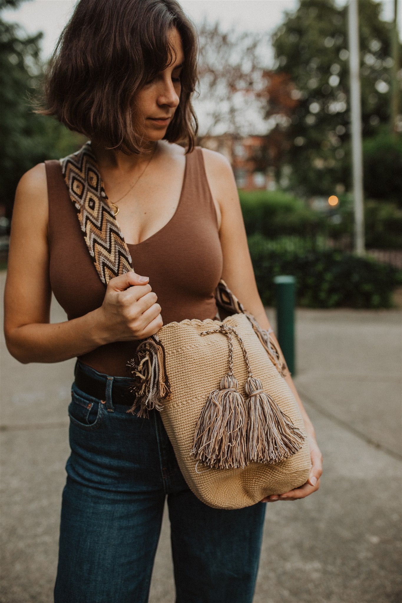 Woman with brown hair standing in park showing cream color crochet crossbody boho bag.