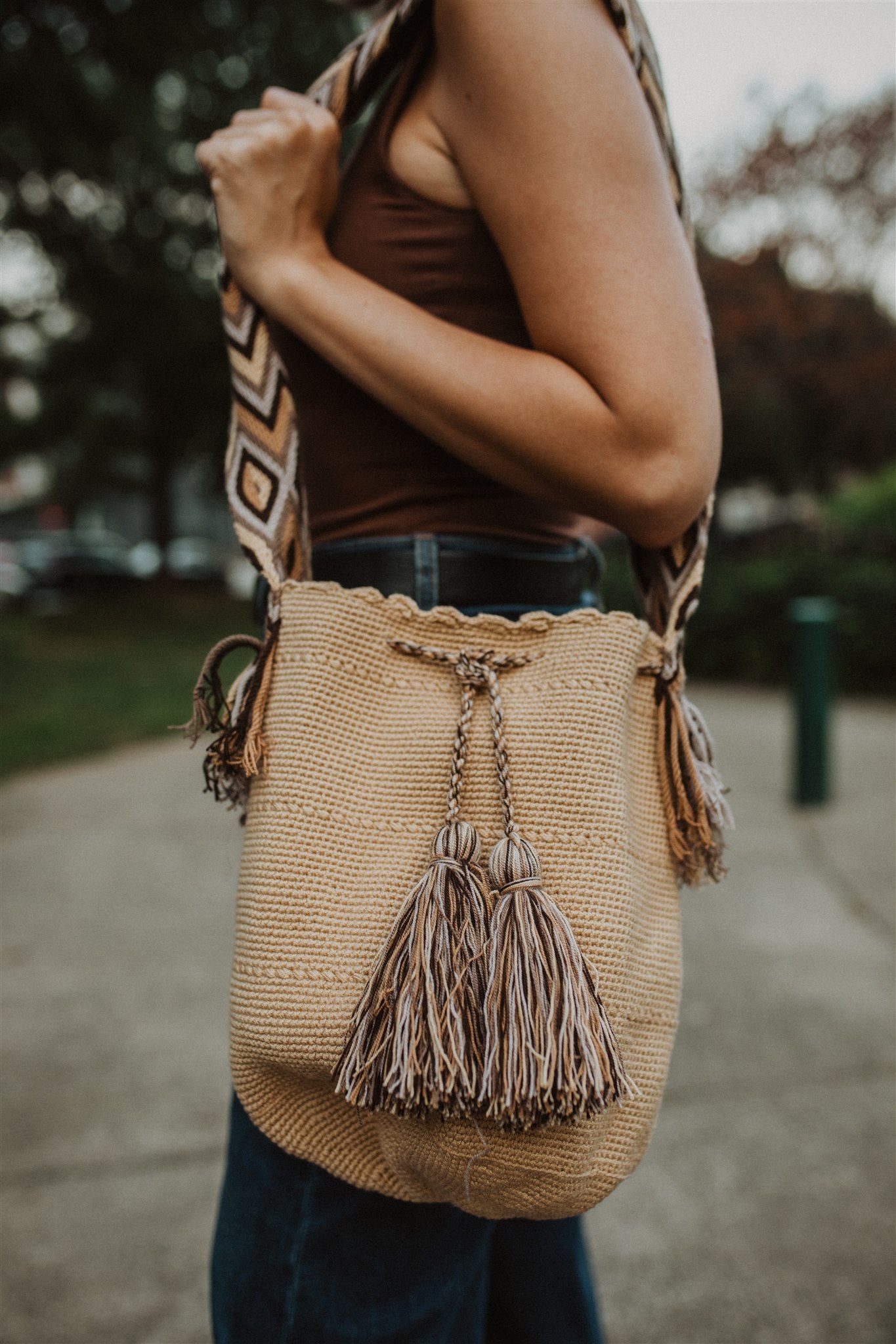 Woman standing in park, sideways to camera wearing cream shoulder bag with brown strap.