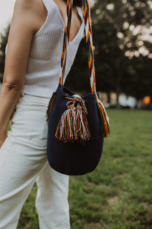 Woman in white standing in park with navy blue crochet shoulder bag and colorful strap.