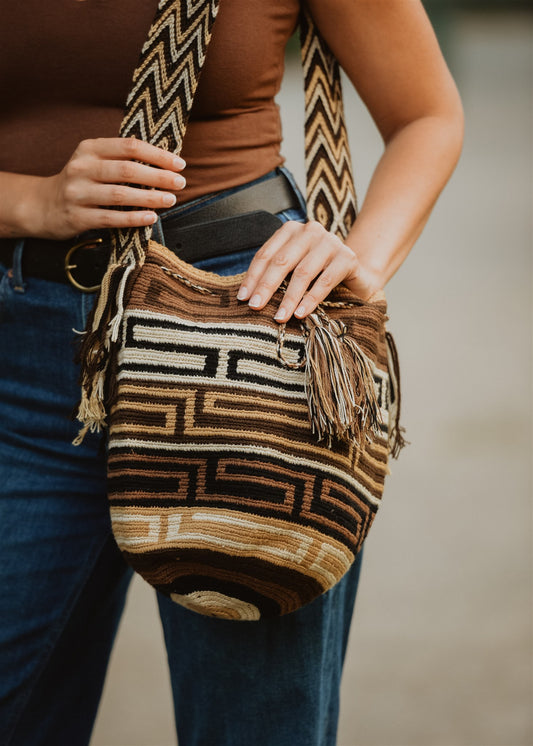 Closeup of brown patterned crochet shoulder bag held by woman in blue jeans.