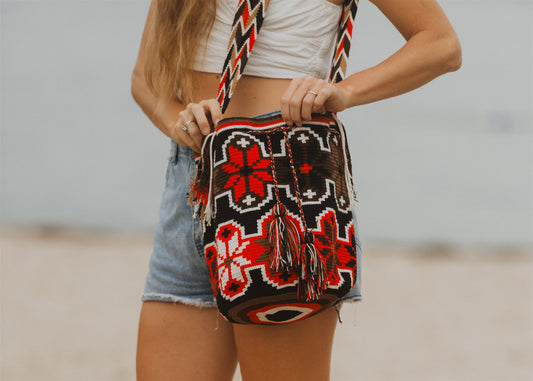 Woman in denim shorts on beach, closeup of red brown white crochet shoulder tote bag.