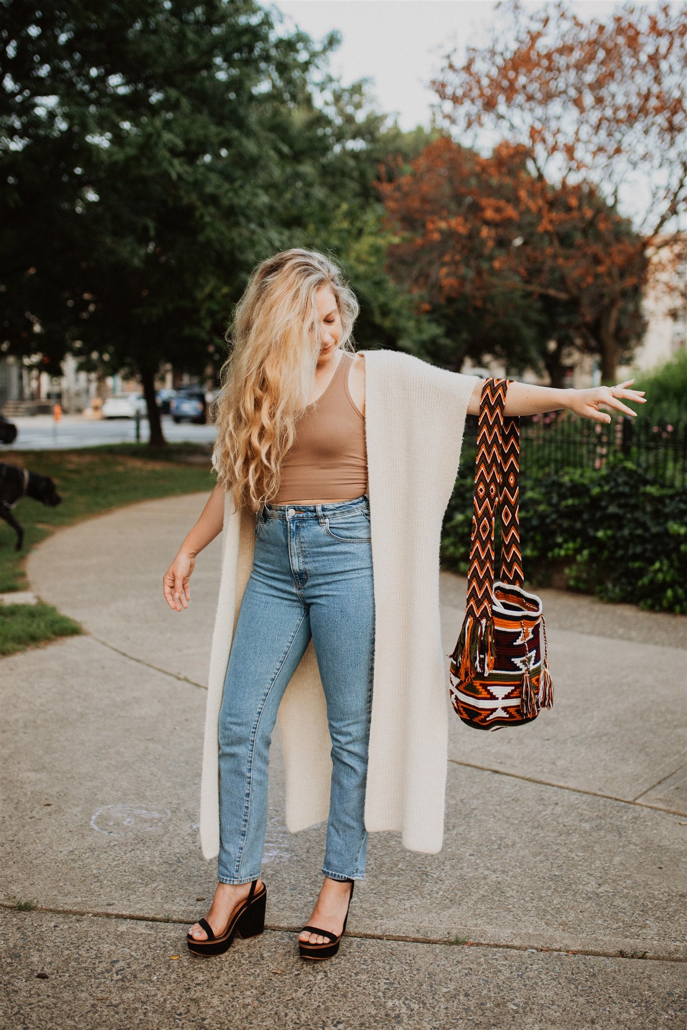 Blonde woman standing in park holding orange maroon cute crochet crossbody bag.