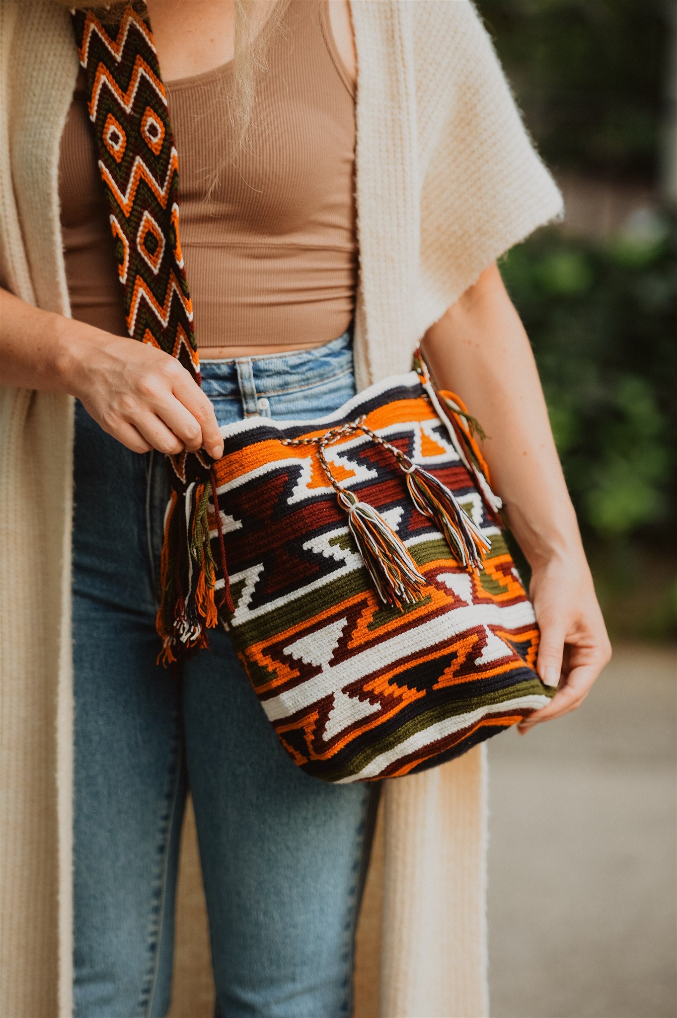 Woman in blue jeans showing colorful crochet shoulder bag.